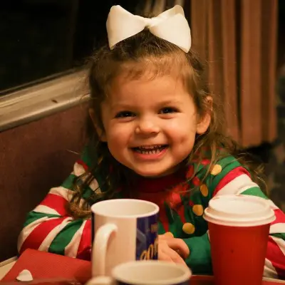 a little girl sitting at a table with a cup of coffee
