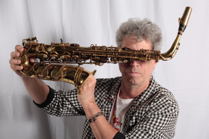 Man holding a saxophone vertically in front of face with a white background.