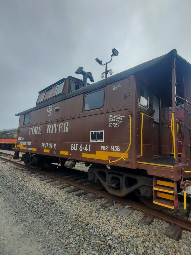 Brown caboose train car on railway tracks under a cloudy sky.