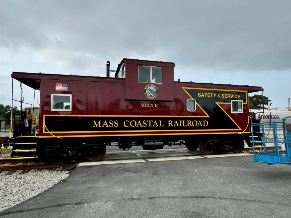 Red Mass Coastal Railroad caboose with American flag and safety slogans.