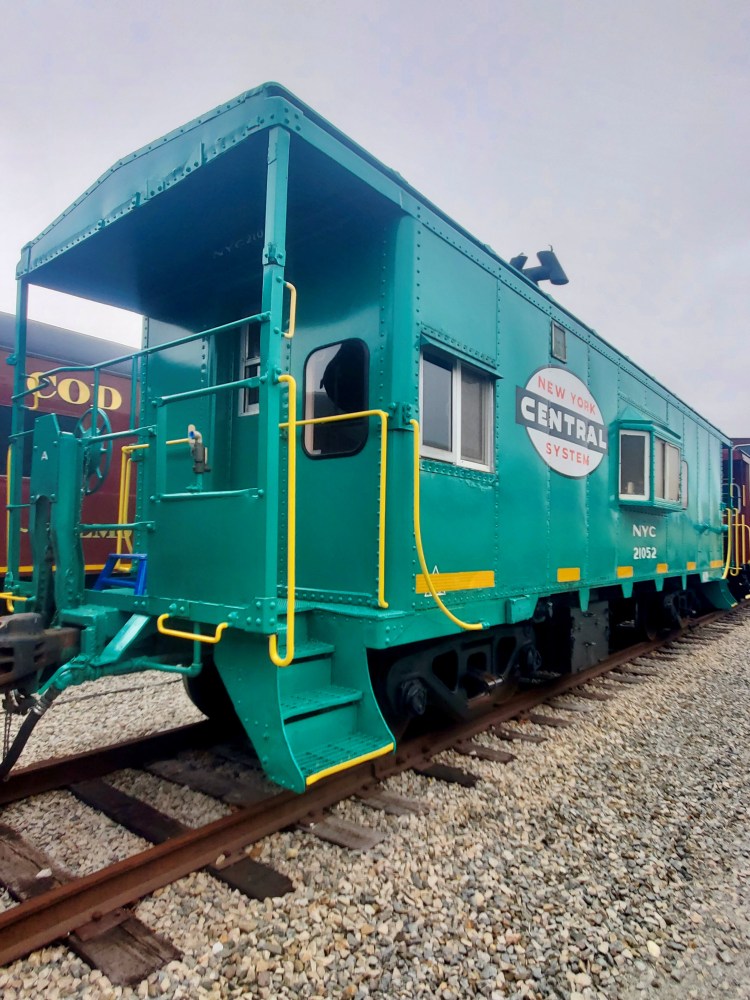 Green vintage train car with 'New York Central System' logo on railway tracks.