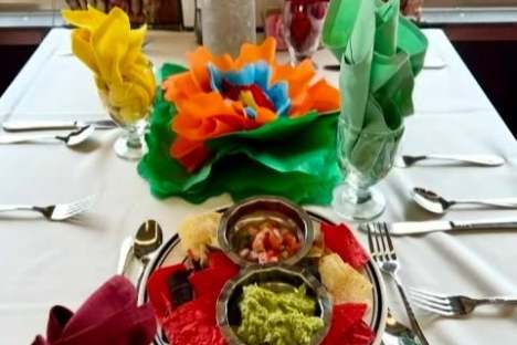 Colorful table setting with chips and dip on a white tablecloth.