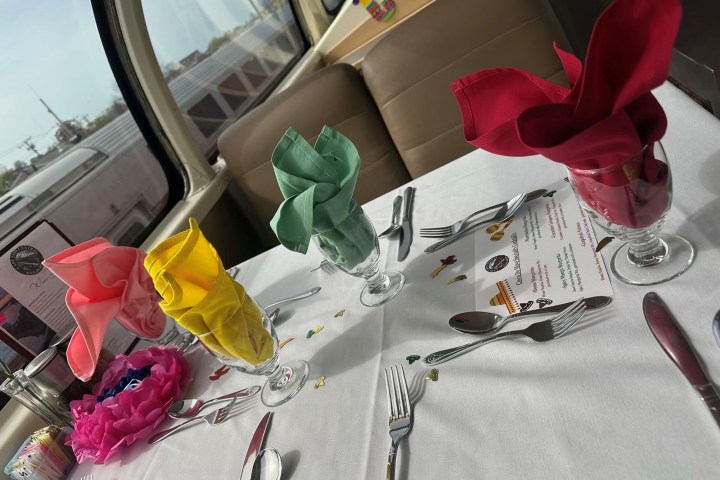 Table set with colorful napkins, cutlery, and glassware on white cloth.