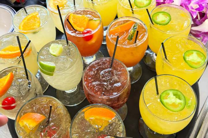 Tray of colorful cocktails with garnishes like fruit and jalapeño slices.