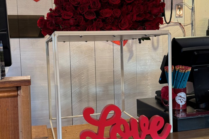 A bouquet of red roses next to a red 'Love' sign on a wooden counter.