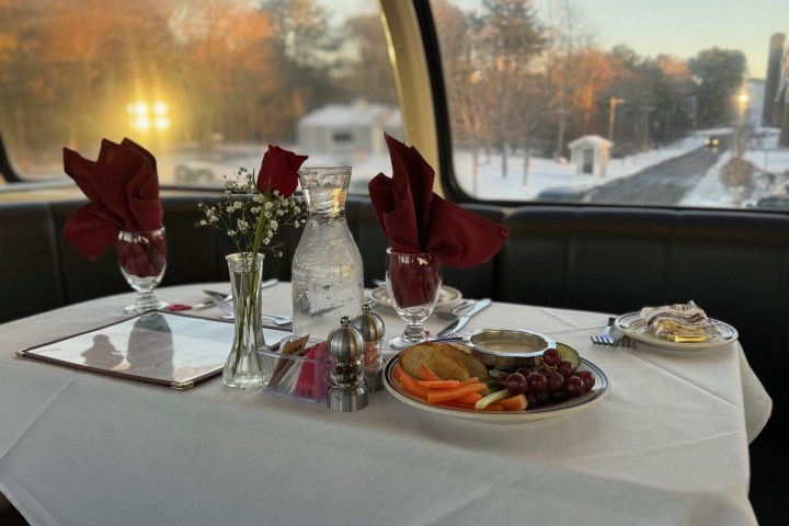 Table set for dining with red napkins, flowers, water, and plates of food by large window.