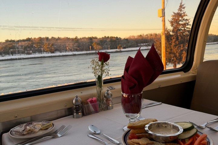 Table with snacks and rose on a train, scenic view outside window.