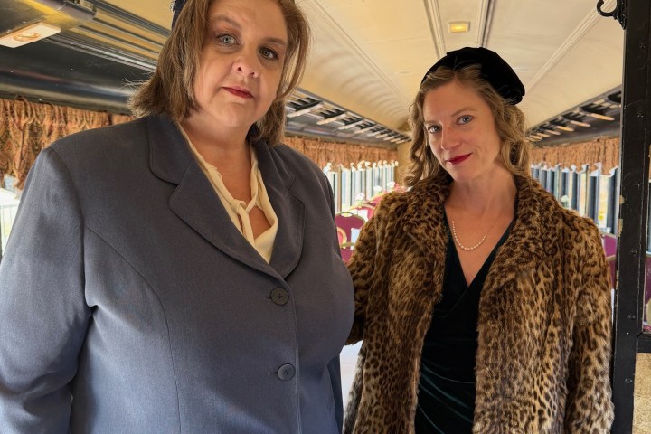 Two women in vintage attire posing inside a train carriage.