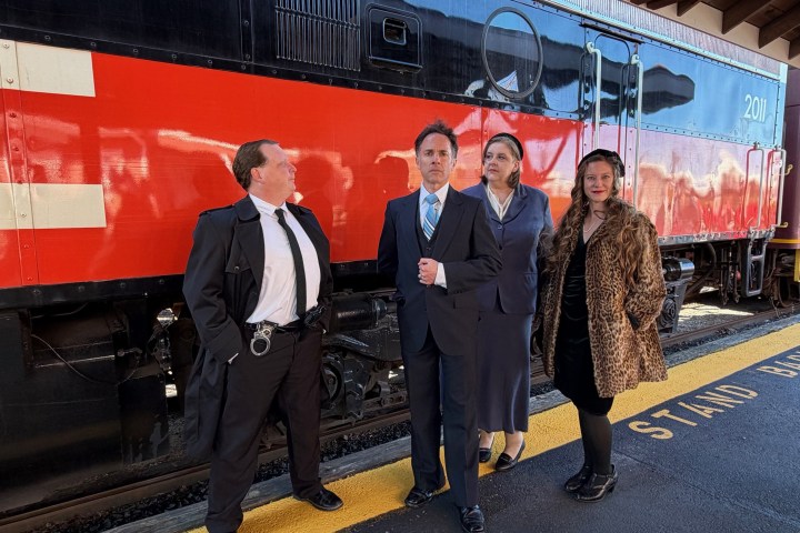 Four people in vintage attire pose in front of a red and black train.