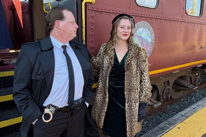 Two people in vintage attire standing by a red train car.